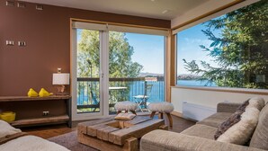 Uma sala de estar moderna com uma mesa de centro de madeira, um sofá e vista para um lago através de grandes janelas.