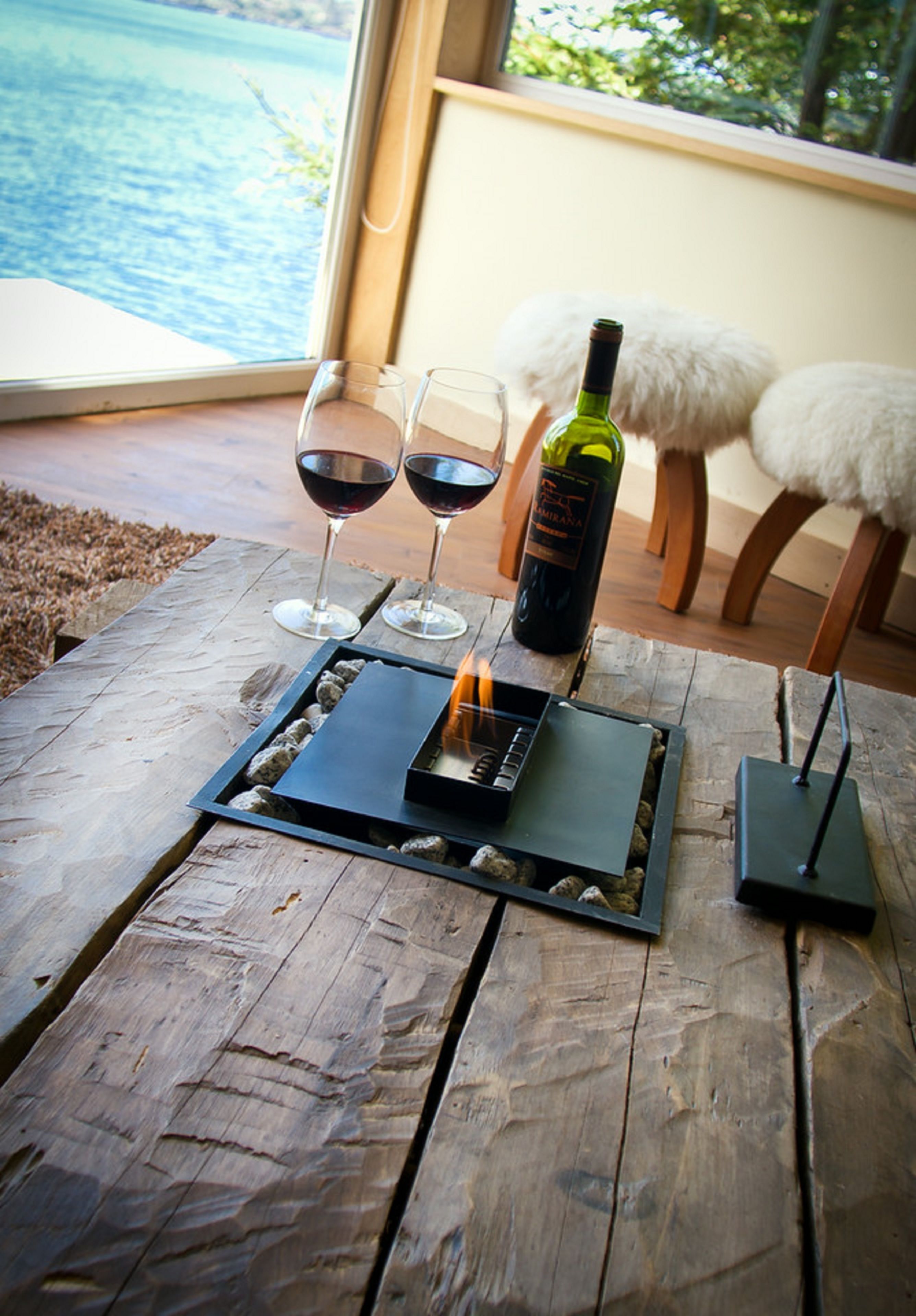A wooden table with two glasses of red wine, a bottle of wine, and a portable grill.