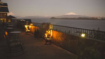 A terrace with outdoor seating and a fire feature, overlooking a body of water and distant mountains.
