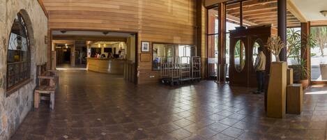 A spacious lobby with a wooden reception desk, a check-in counter, and a large glass door leading outside.