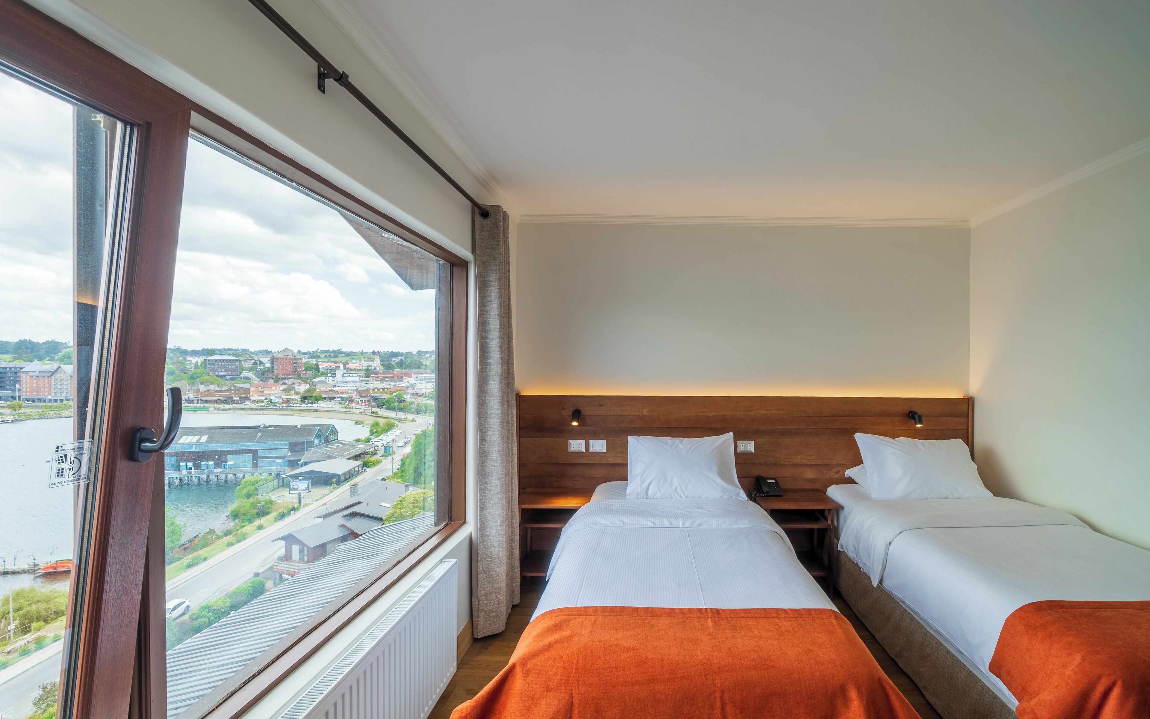 A hotel room with two beds, a view of a cityscape, and a window with a view of a river.