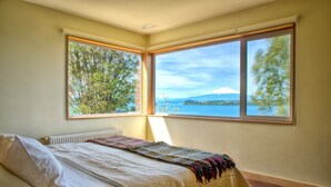 Quarto com cama, radiador e janela ampla com vista para um lago e montanha.