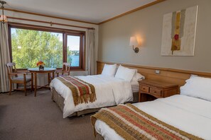 Une chambre d’hôtel avec deux lits, une tête de lit en bois, une table de chevet, une petite table avec des chaises et une fenêtre avec des rideaux.