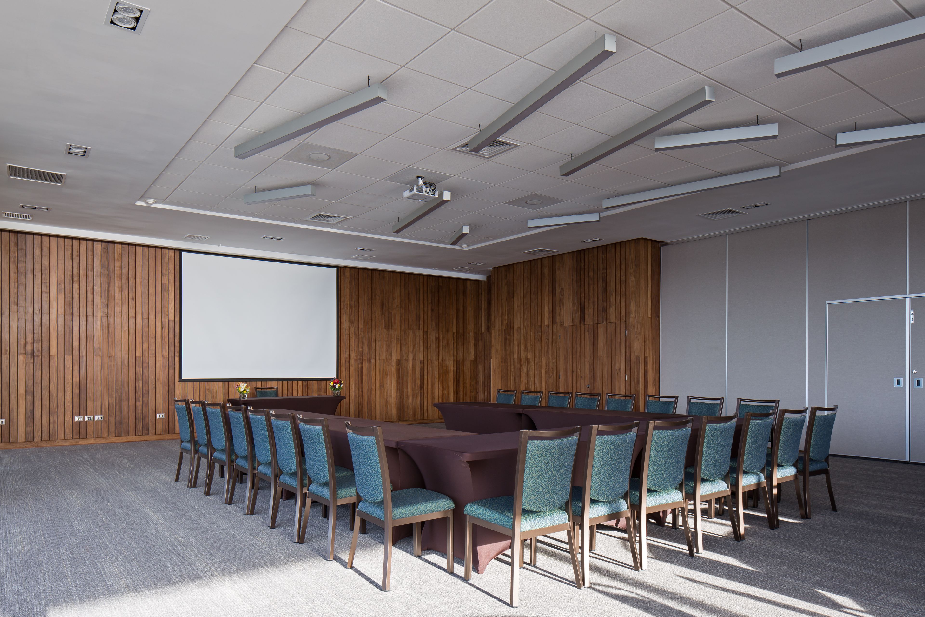A conference room with a large table and chairs, a projector screen, and a wooden panel wall.