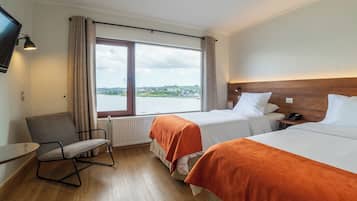 Habitación de hotel con dos camas, una silla, televisión y ventana con vista al agua y edificios.