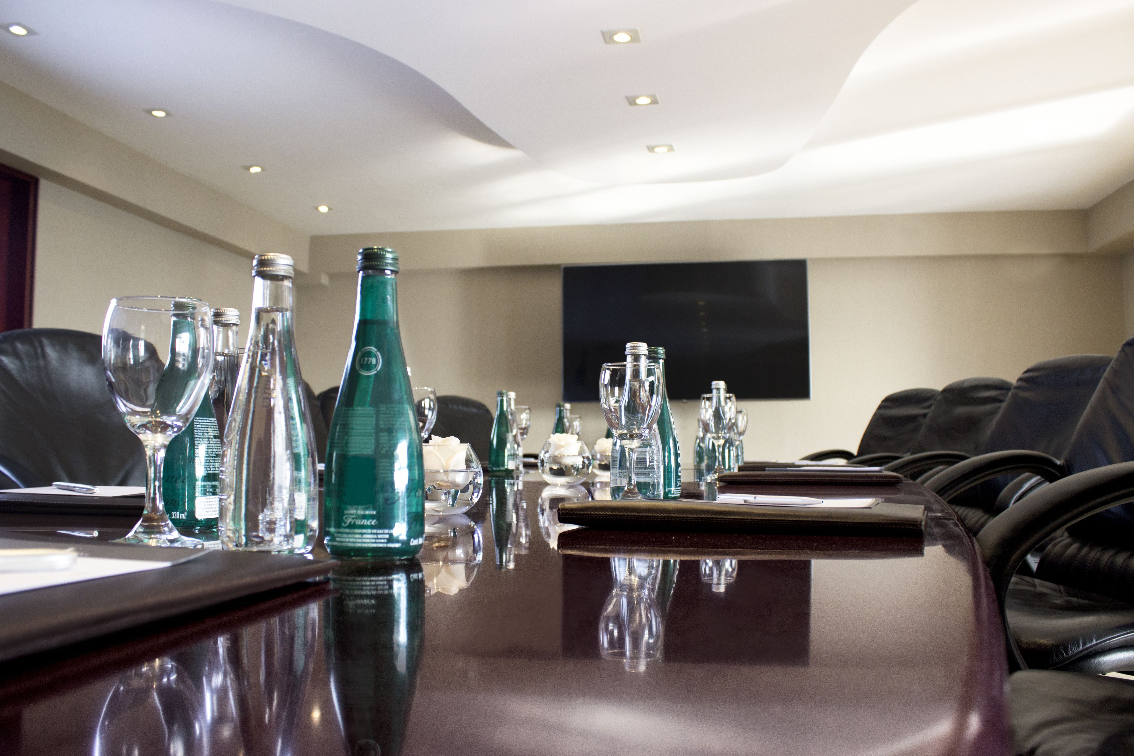 Un salón de conferencias con una larga mesa, sillas, diferentes vasos y botellas.