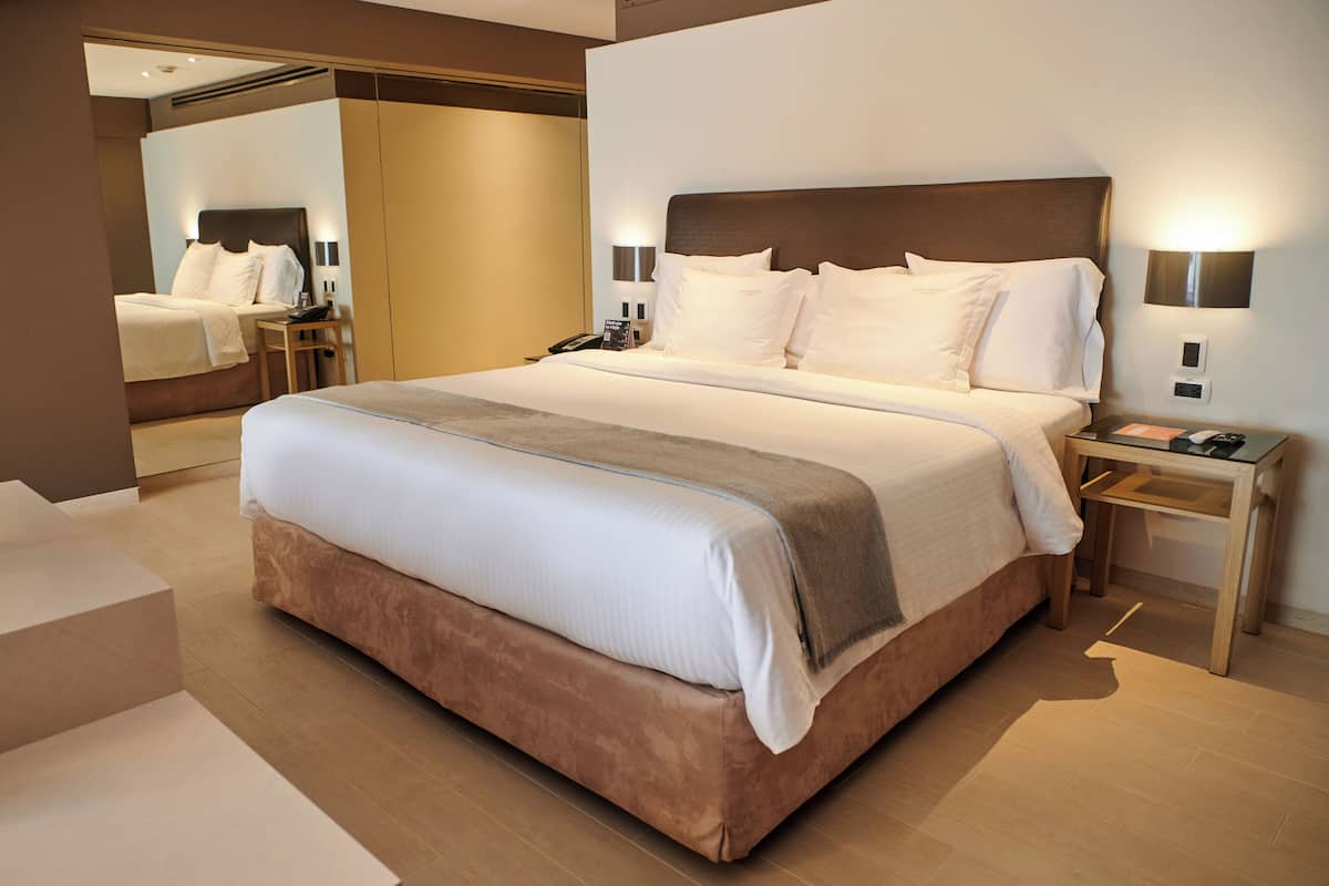 A modern hotel room with a large bed, bedside tables, a mirror, and a nightstand.