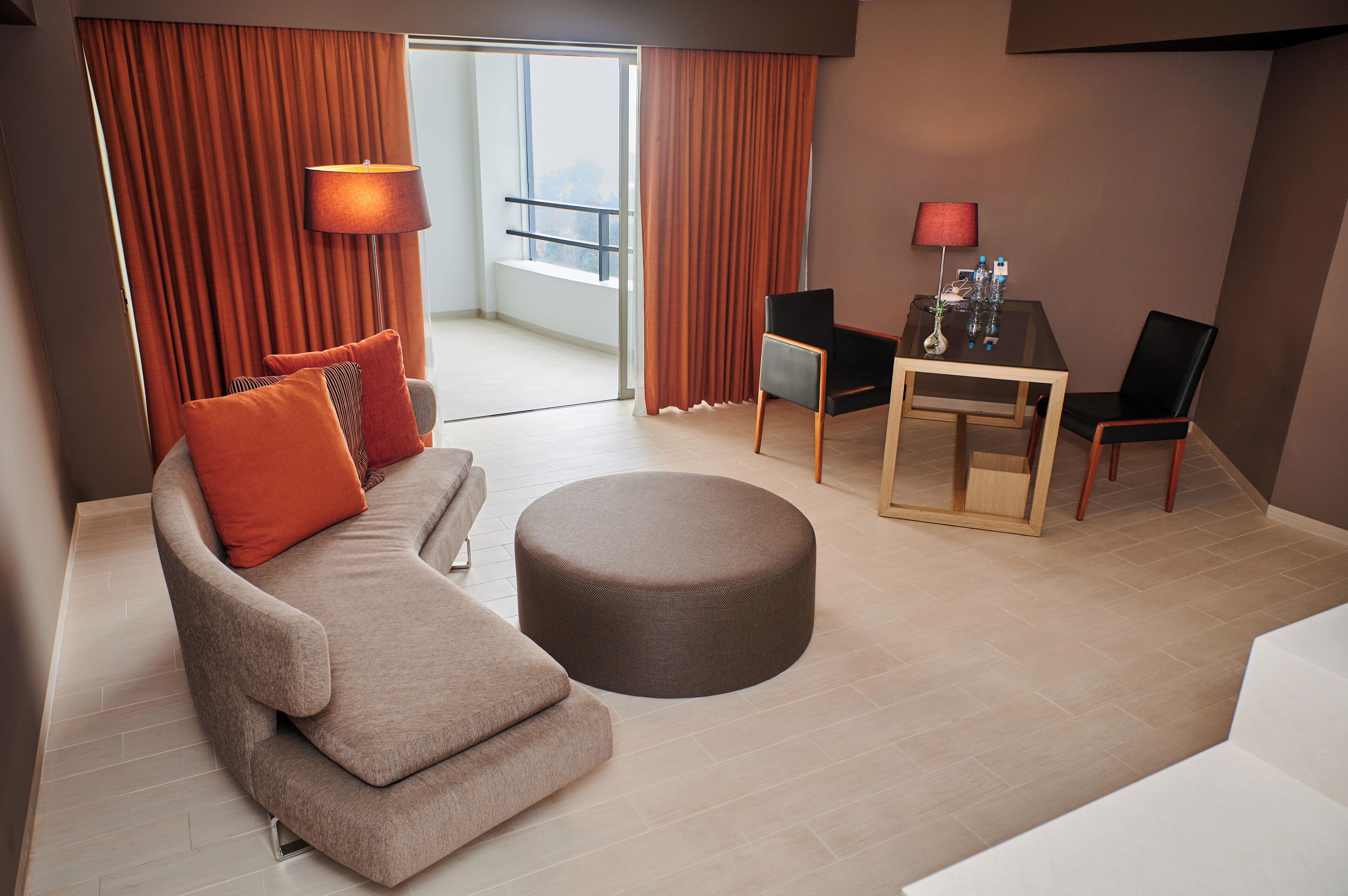 Una habitación de hotel moderna con sofá, reposapiés y una mesa de comedor con sillas.
