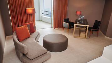 Una habitación de hotel moderna con sofá, reposapiés y una mesa de comedor con sillas.