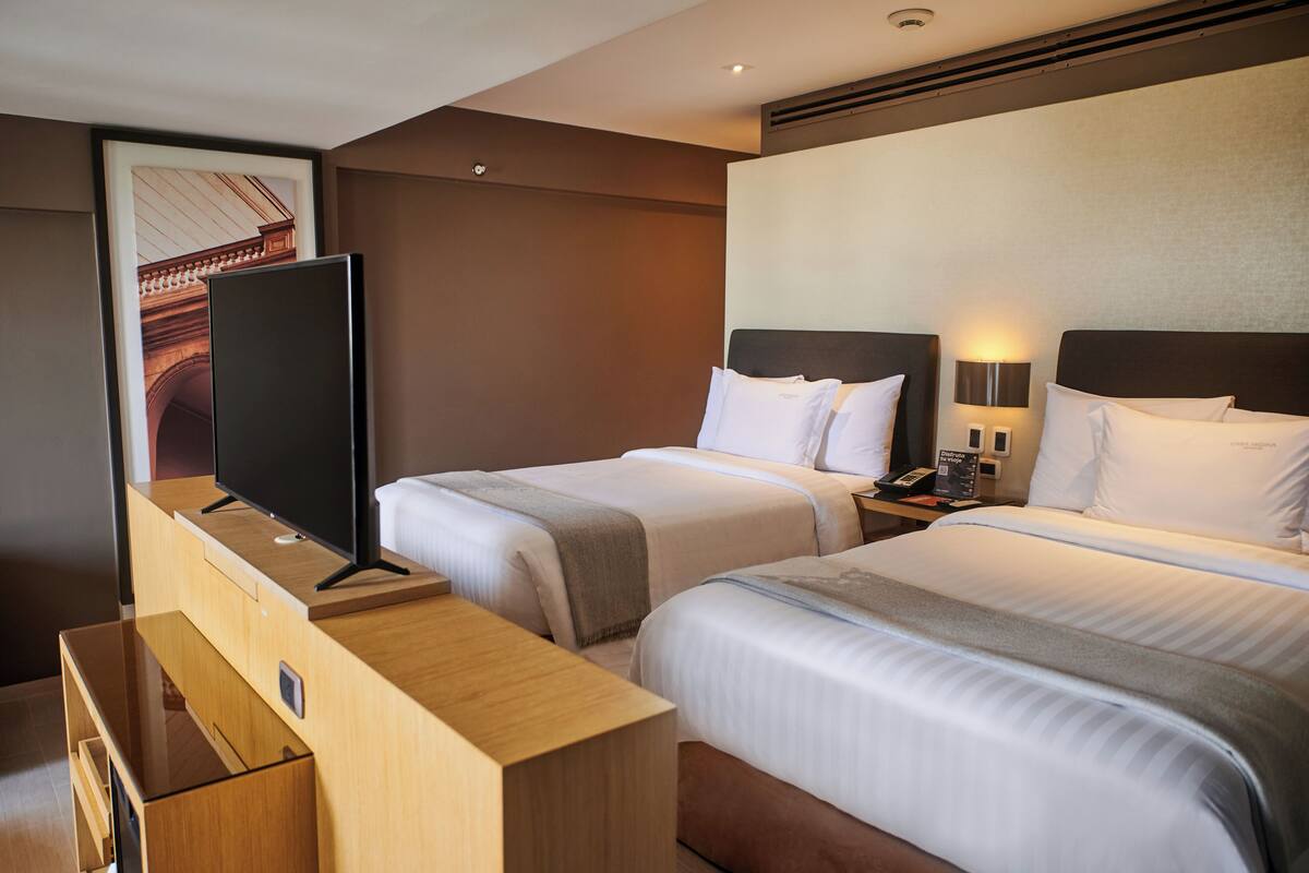 A hotel room with two beds, a TV, and a desk with drawers.
