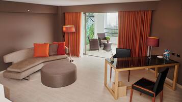A modern living room with a sofa, ottoman, dining table, and chairs. There is a balcony with curtains and a view of greenery.
