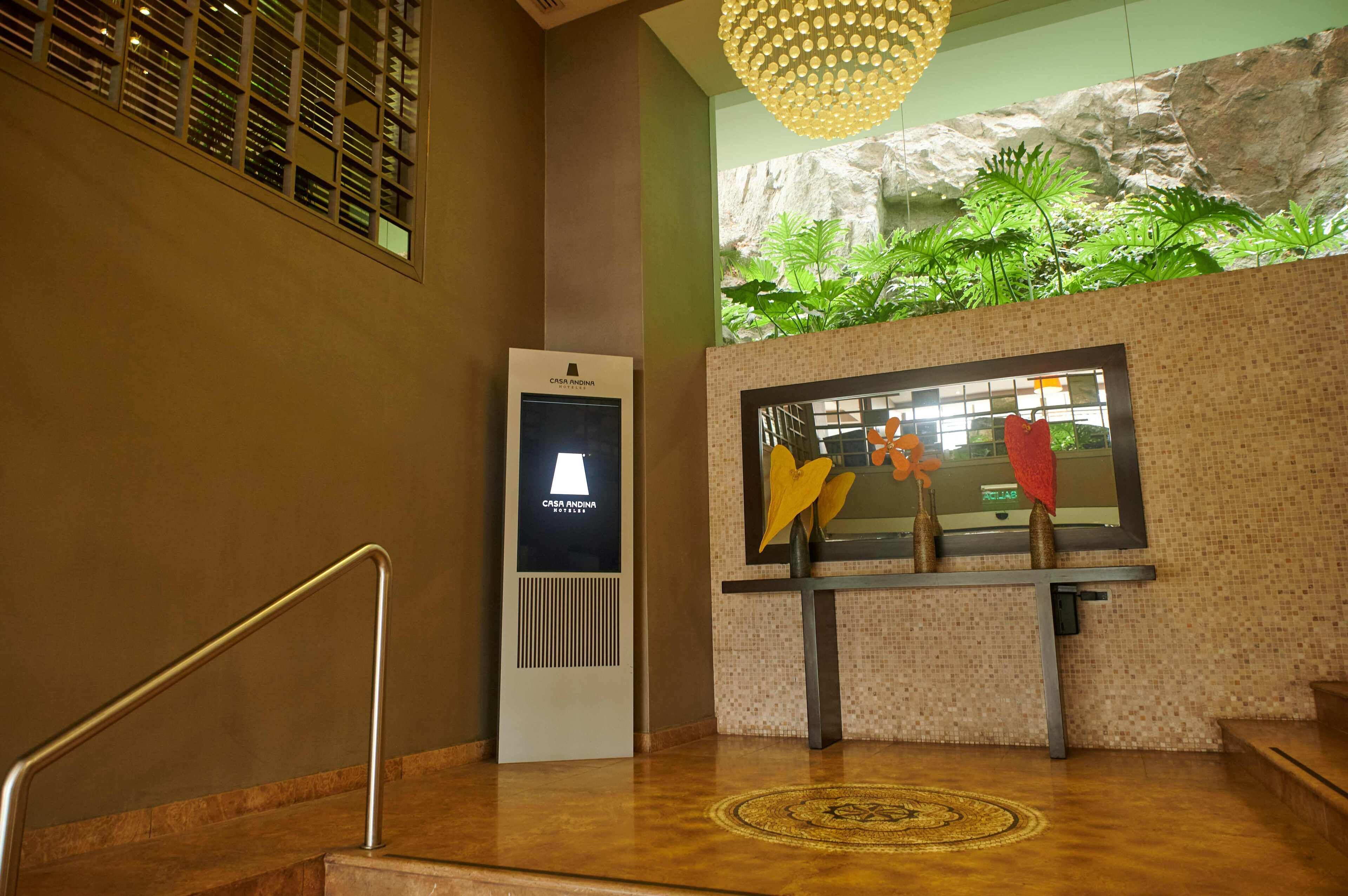 A hotel lobby with a reception desk, a staircase with a handrail, a decorative wall with a rock-like texture, and a hanging light fixture.