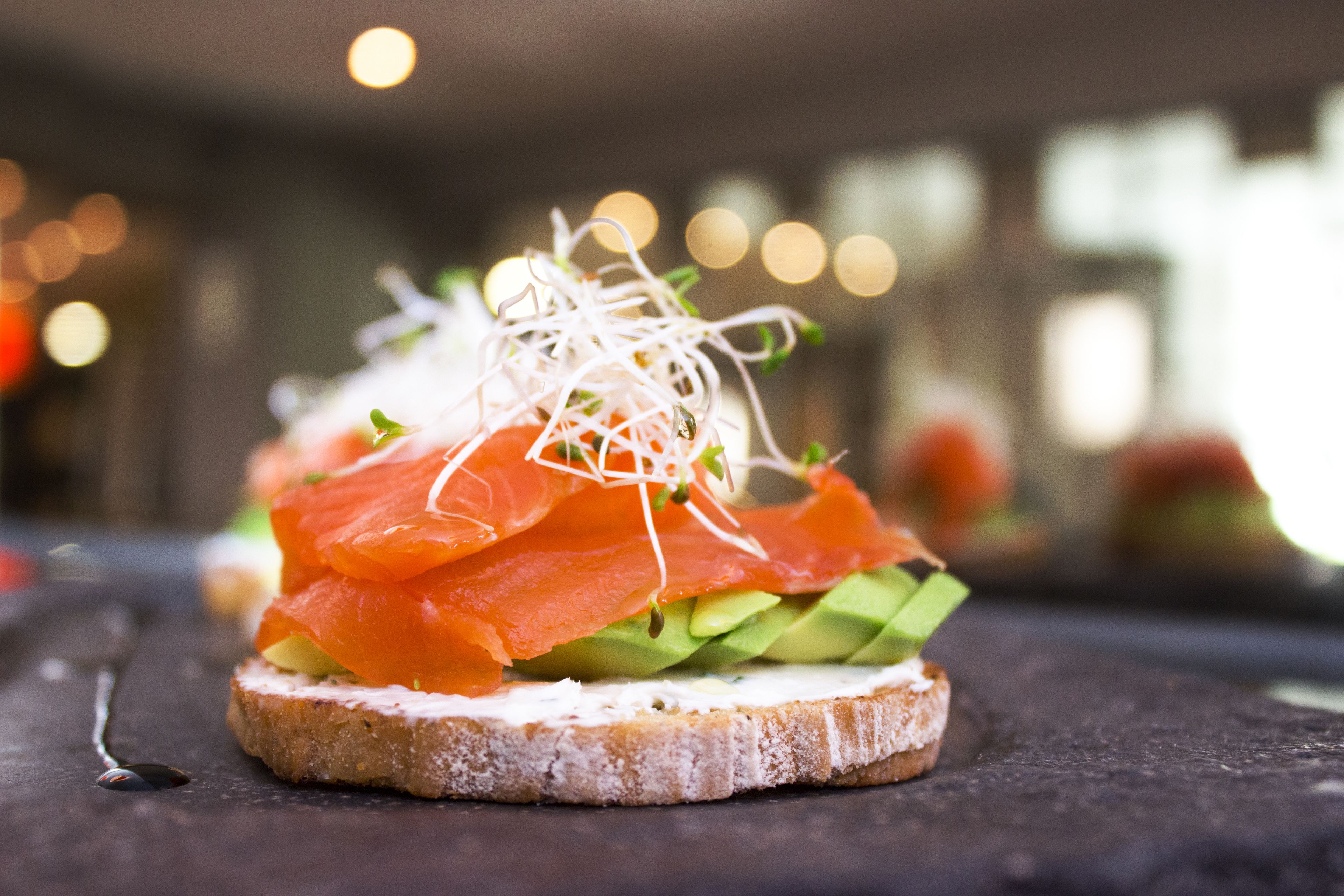 A sandwich with smoked salmon, avocado, and sprouts on a slice of bread.