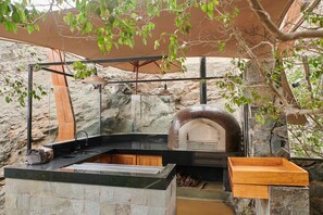 Un espace cuisine extérieur carrelé, doté d’un four à pizza encastré, d’un évier et d’un plan de travail en bois.