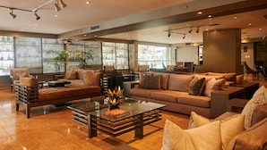 A spacious living area with a sofa, armchairs, and a coffee table. There are large windows with blinds, a plant, and a fireplace. - Casa Andina Premium Golf Los Incas (Santiago de Surco)
