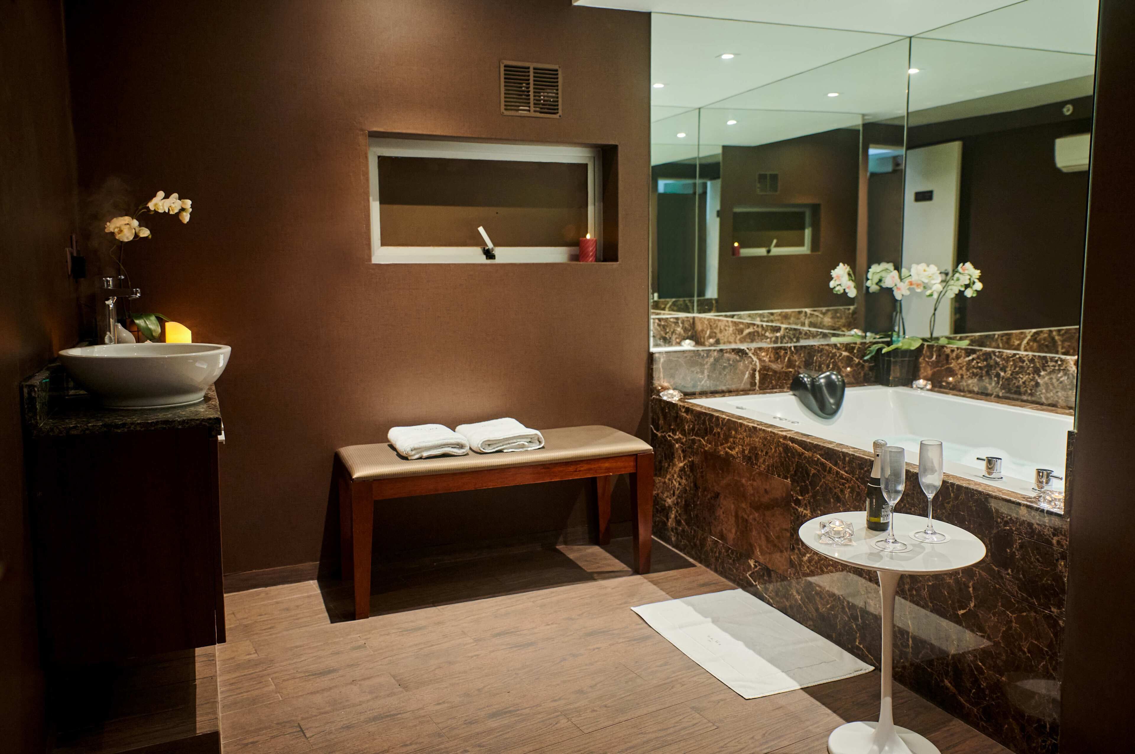 A modern bathroom with a marble sink, a bench, a small table with two glasses, and a large mirror.