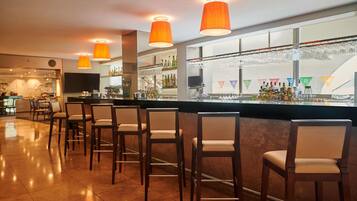 Zona de bar con sillas de madera, mostrador con vitrina de vidrio y lámparas colgantes naranjas.