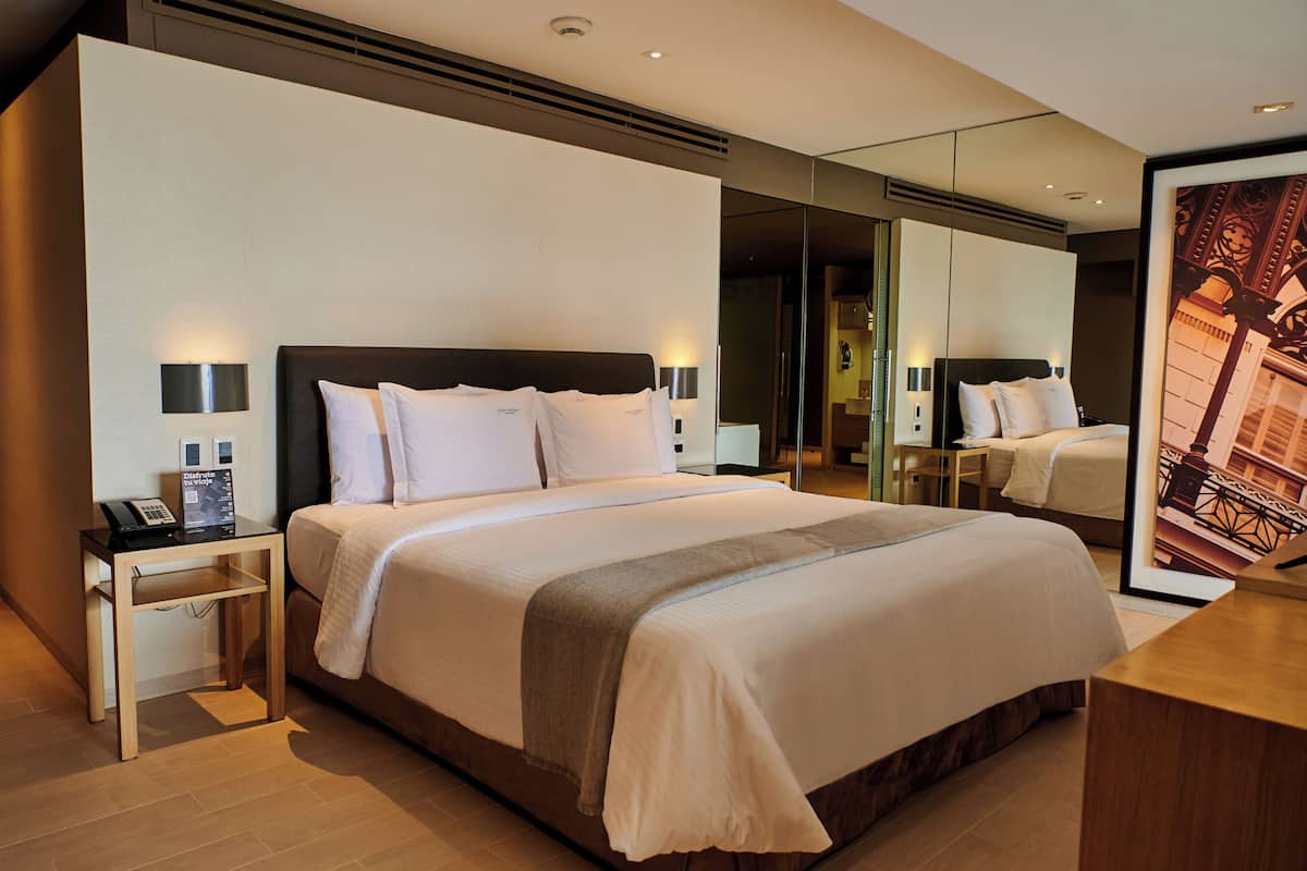A modern hotel room with a large bed, bedside tables, a mirror, and a framed picture on the wall.