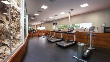 Un gimnasio con cintas de correr, bicicletas estáticas y un amplio ventanal con vistas a zonas verdes.