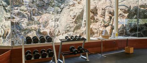 A gym with weightlifting equipment and a large window overlooking a rocky outdoor area.