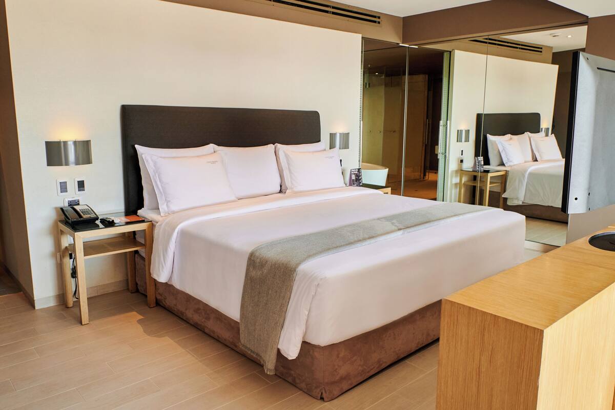 A modern hotel room with a large bed, bedside tables, a mirror, and a wooden desk.