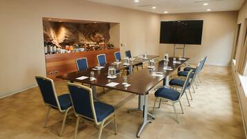 Un salón de conferencias con una larga mesa, sillas azules, una estación de café y una pantalla grande.