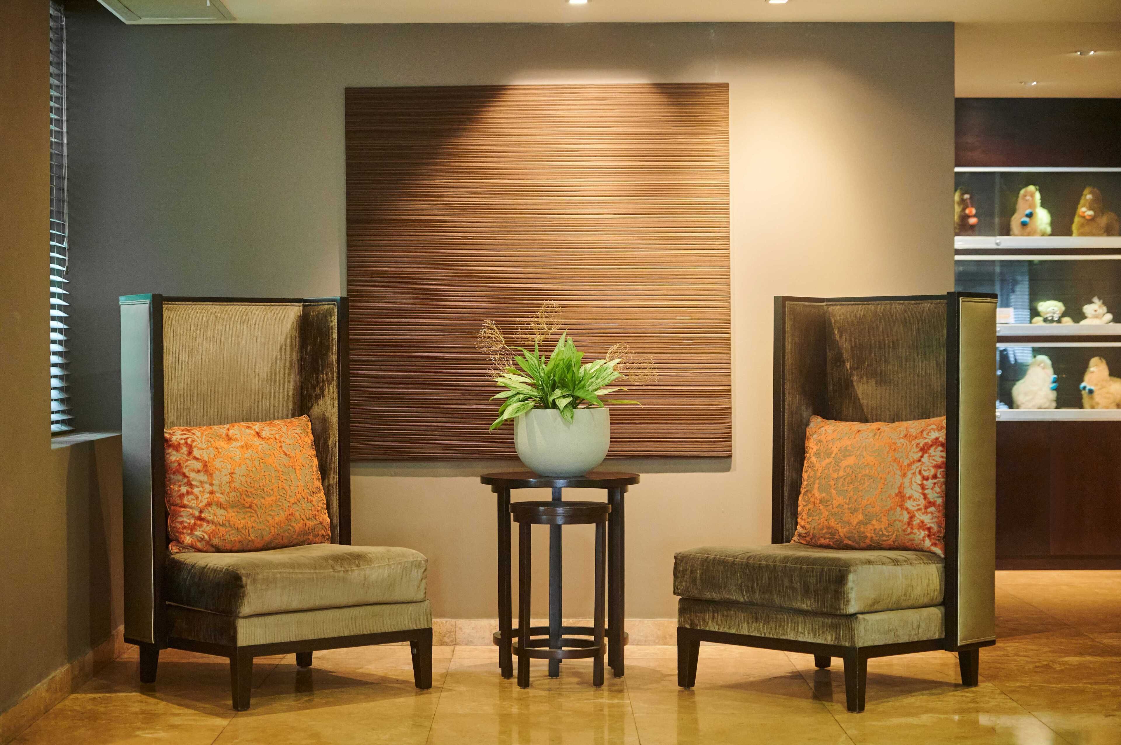 A lobby with two armchairs, a small table with a plant, and a wall with horizontal lines.