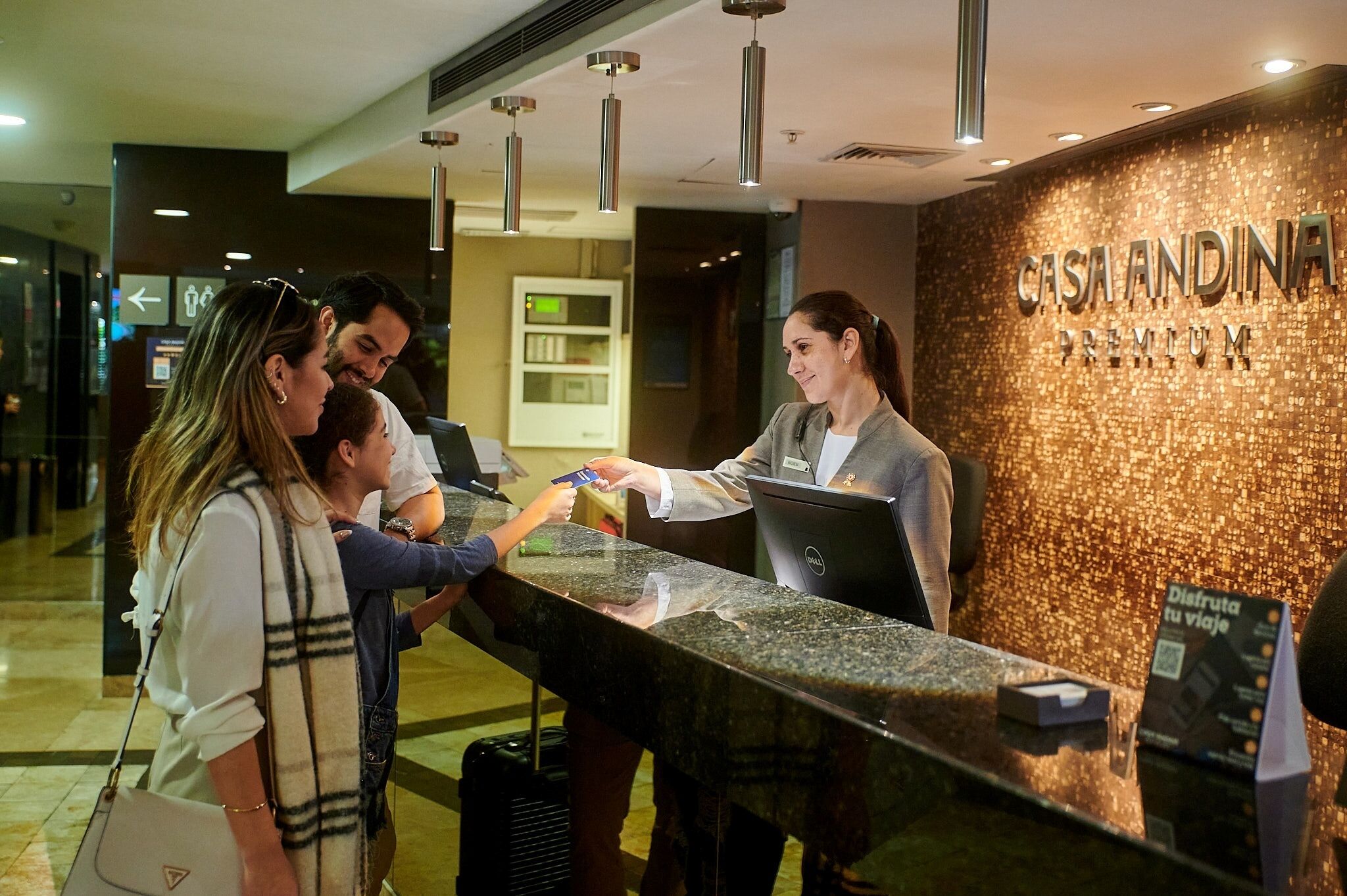 A hotel reception desk with a digital screen, a sign reading "CASA ANDINA PREMIUM," and a person at the counter.