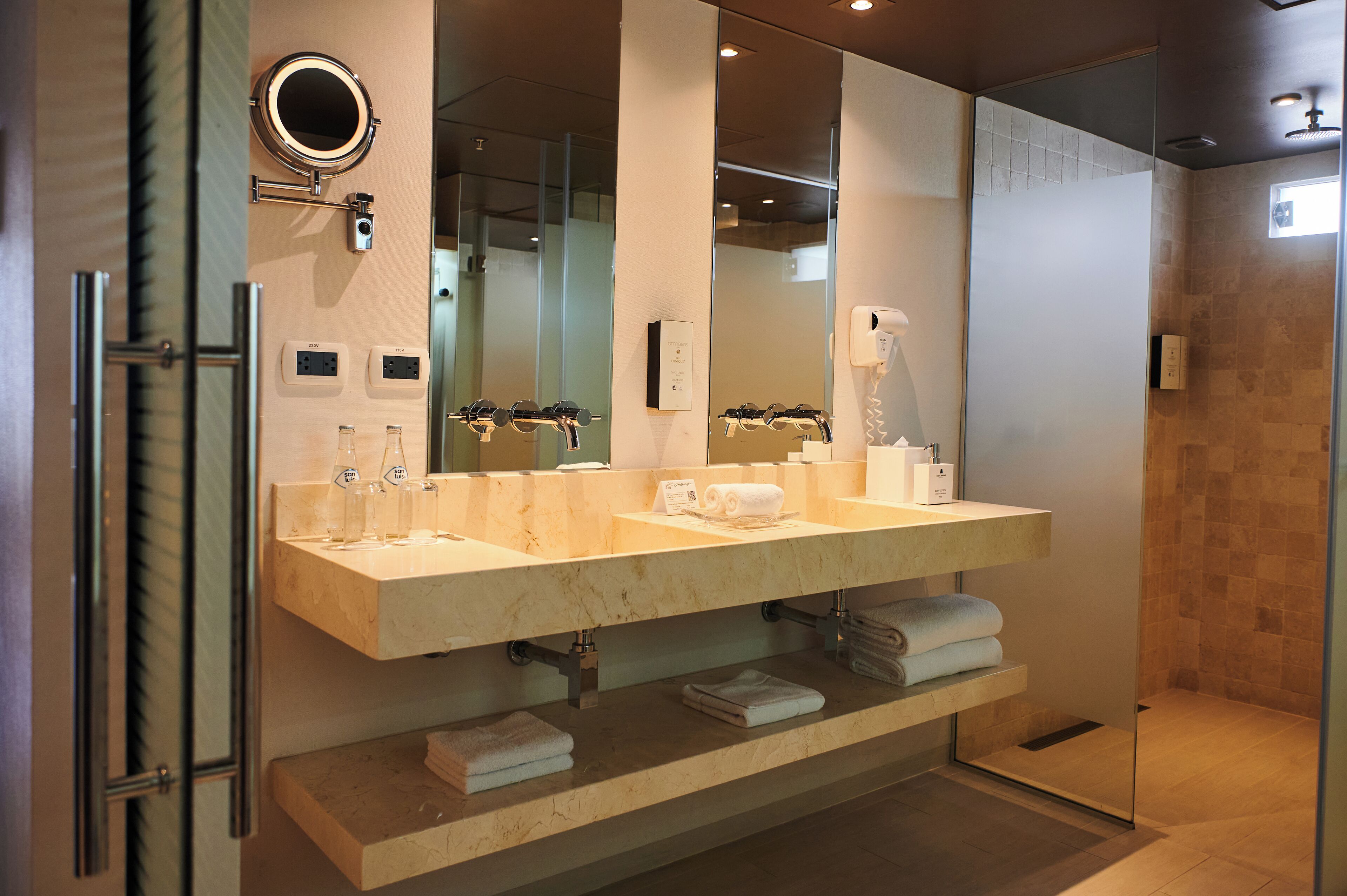 A modern bathroom with a large mirror, dual sinks, and a glass shower enclosure.