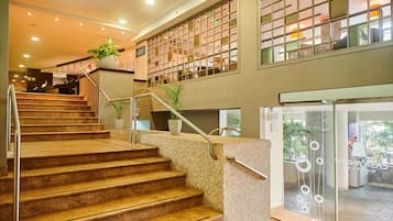 Un vestíbulo de hotel con una escalera, una recepción y una entrada por puerta de cristal.