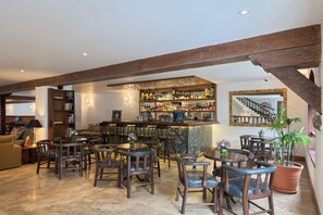 A bar area with wooden chairs and tables, a bar counter with various bottles, and a staircase with a mirror. - La Hacienda Miraflores (Lima)