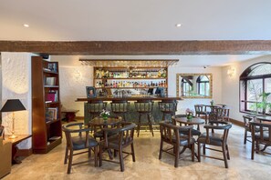 Uma área de bar com móveis de madeira, diversos tipos de garrafas e uma estante de livros.
