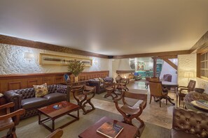 Un vaste espace salon doté de canapés en cuir, de fauteuils en bois et d’une cheminée.