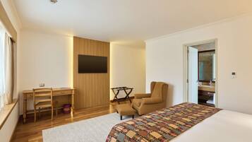 A modern bedroom with a bed, a desk, a chair, and a television.