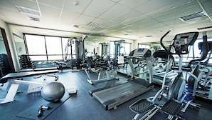 Academia com diversos equipamentos de exercício, incluindo esteiras, bicicleta ergométrica e pesos livres.