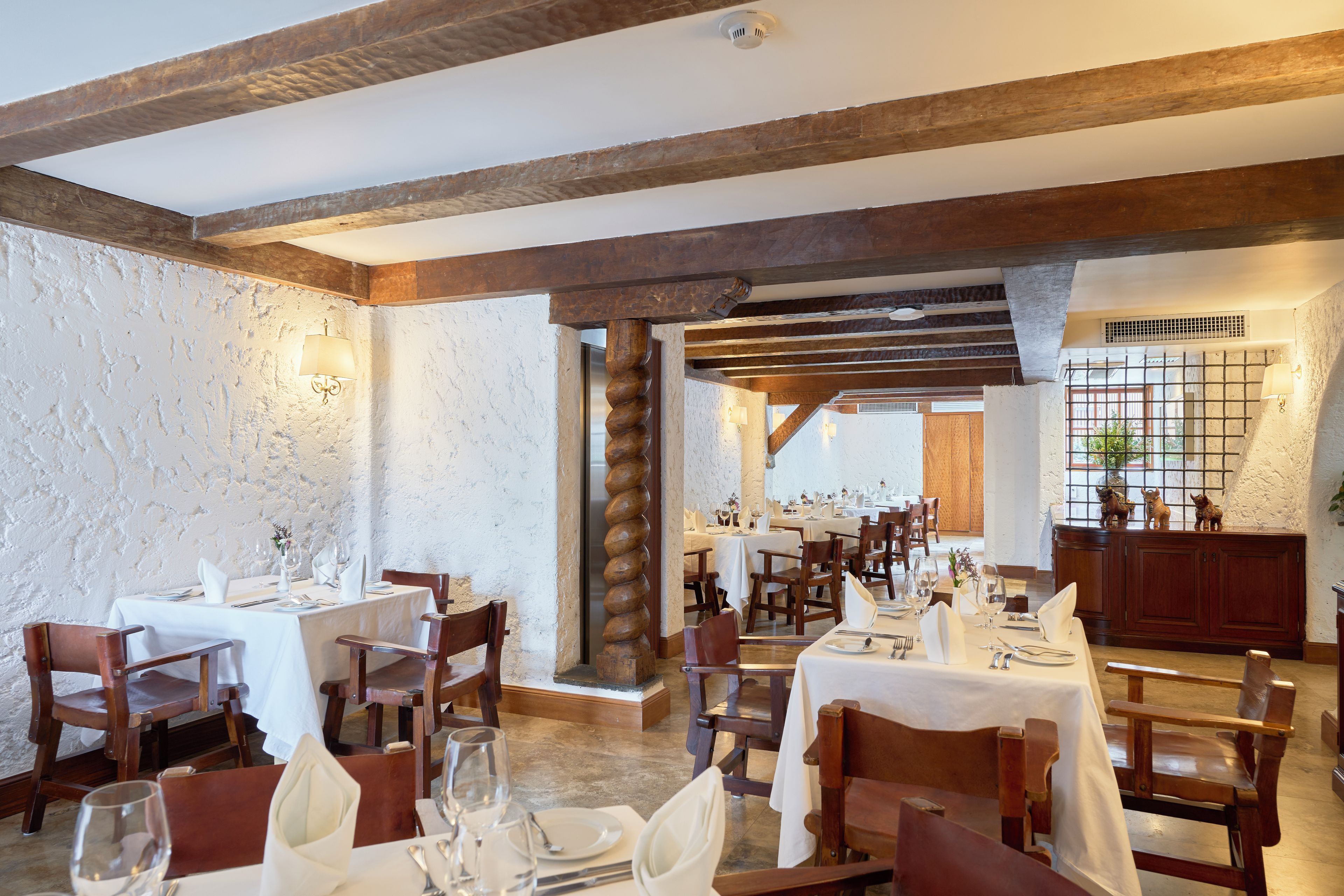 Un restaurante con varias mesas dispuestas para comer, vigas de madera en el techo y una pared de piedra rústica.