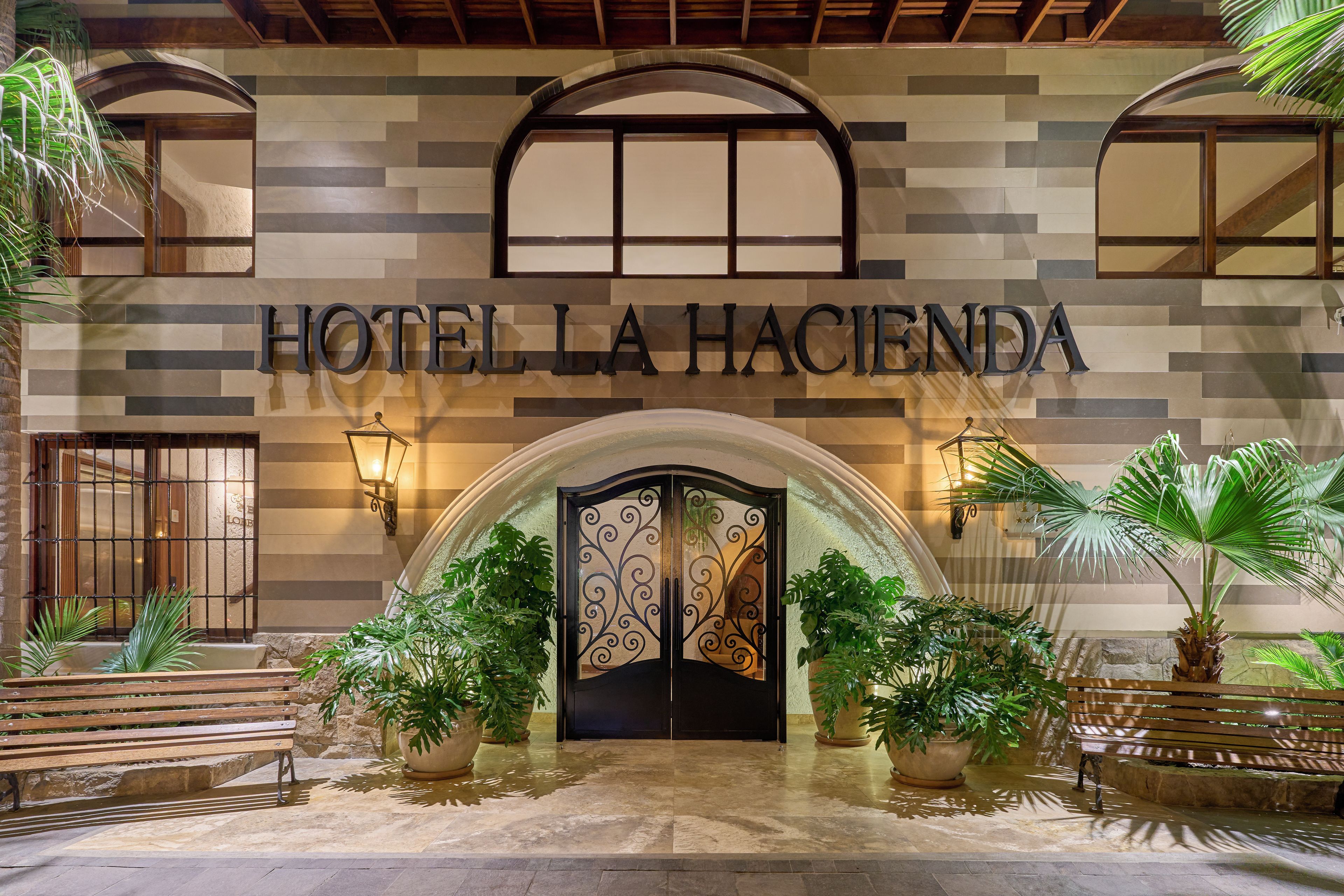 Entrada de un hotel con fachada de azulejos, un amplio arco de entrada y plantas en macetas.