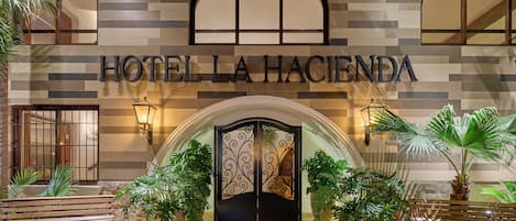 Entrada de un hotel con fachada de azulejos, un amplio arco de entrada y plantas en macetas.