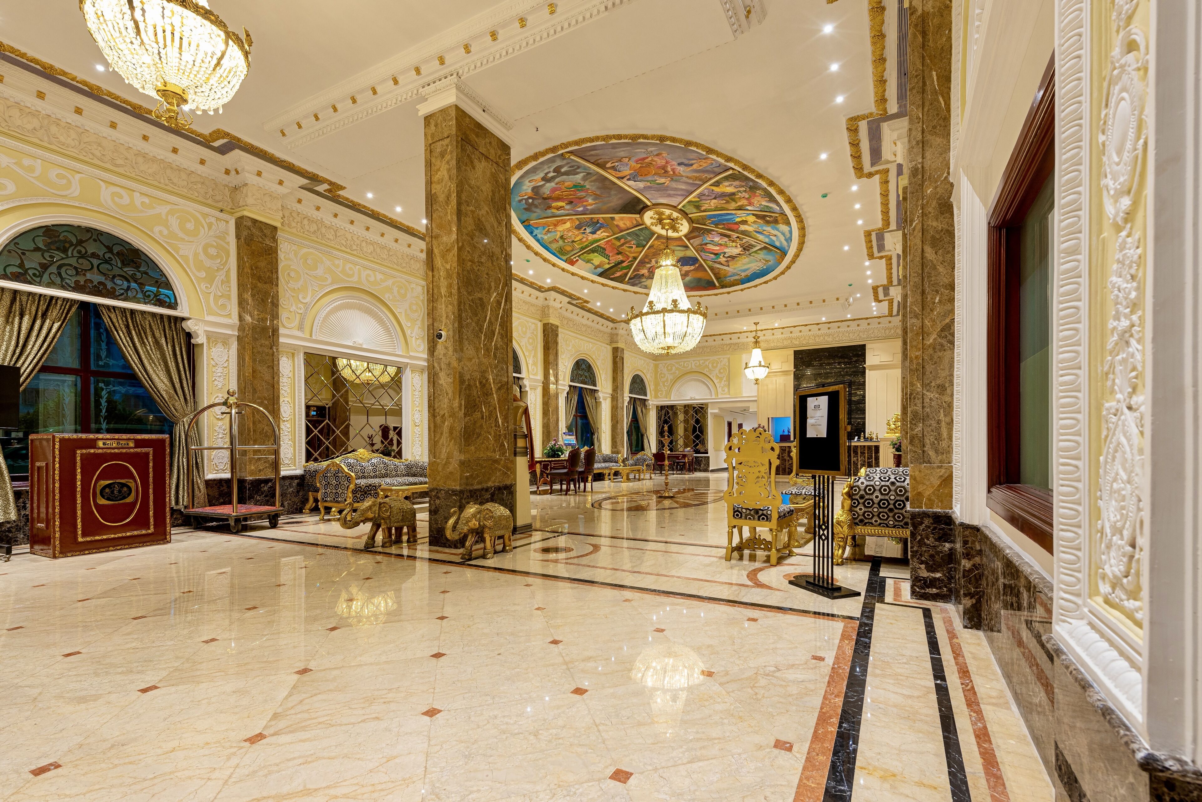 A grand lobby with marble floors, ornate columns, and a large, colorful ceiling mural.