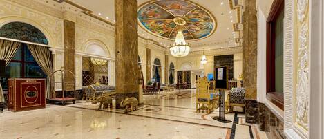A grand lobby with marble floors, ornate columns, and a large, colorful ceiling mural.