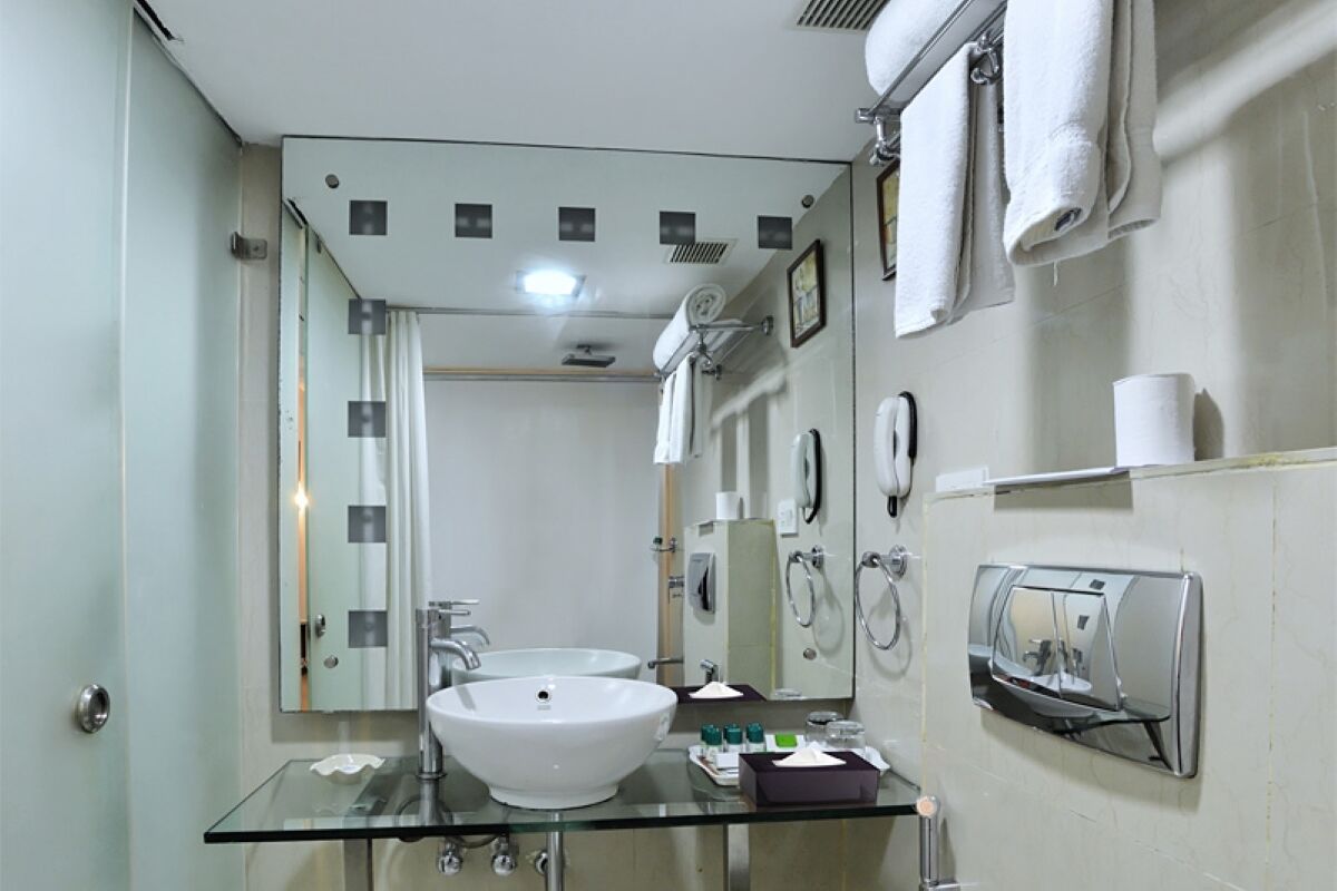 Un baño moderno con lavamanos de vidrio, dos espejos, un toallero y un secador de manos.