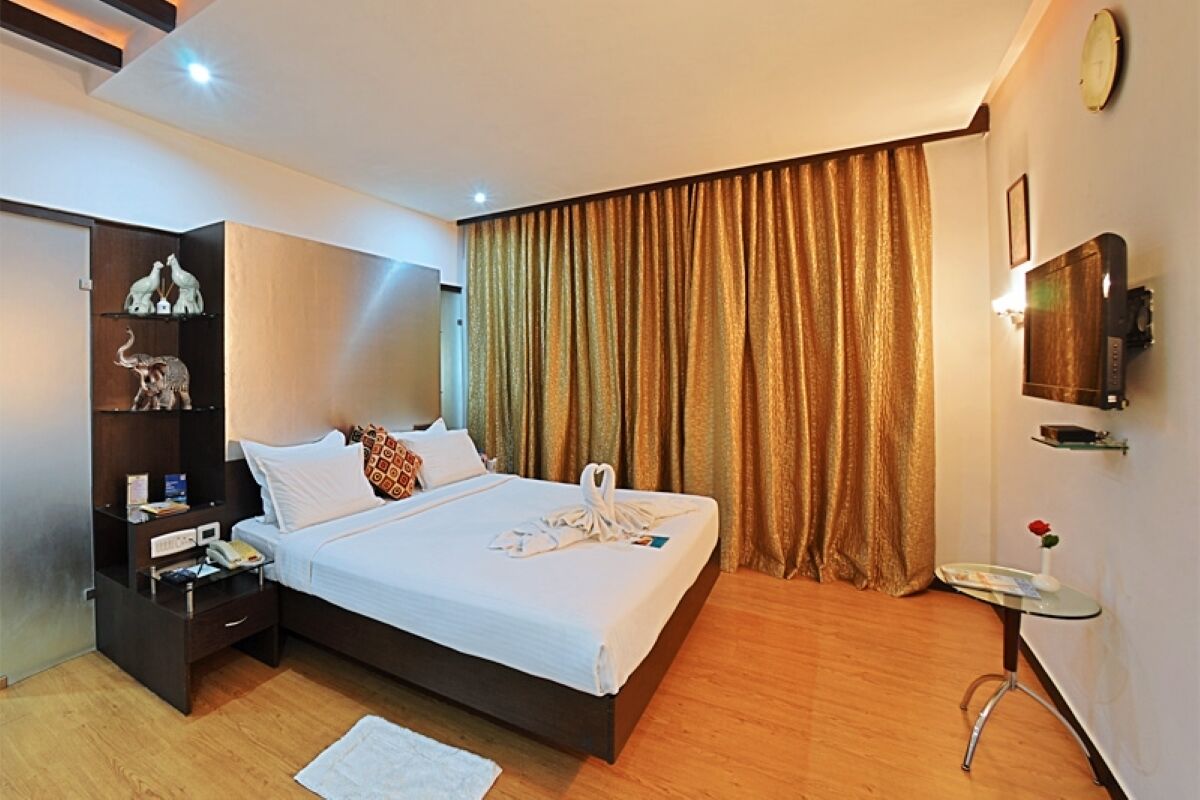 A hotel room with a bed, bedside table, lamp, and a TV mounted on the wall.