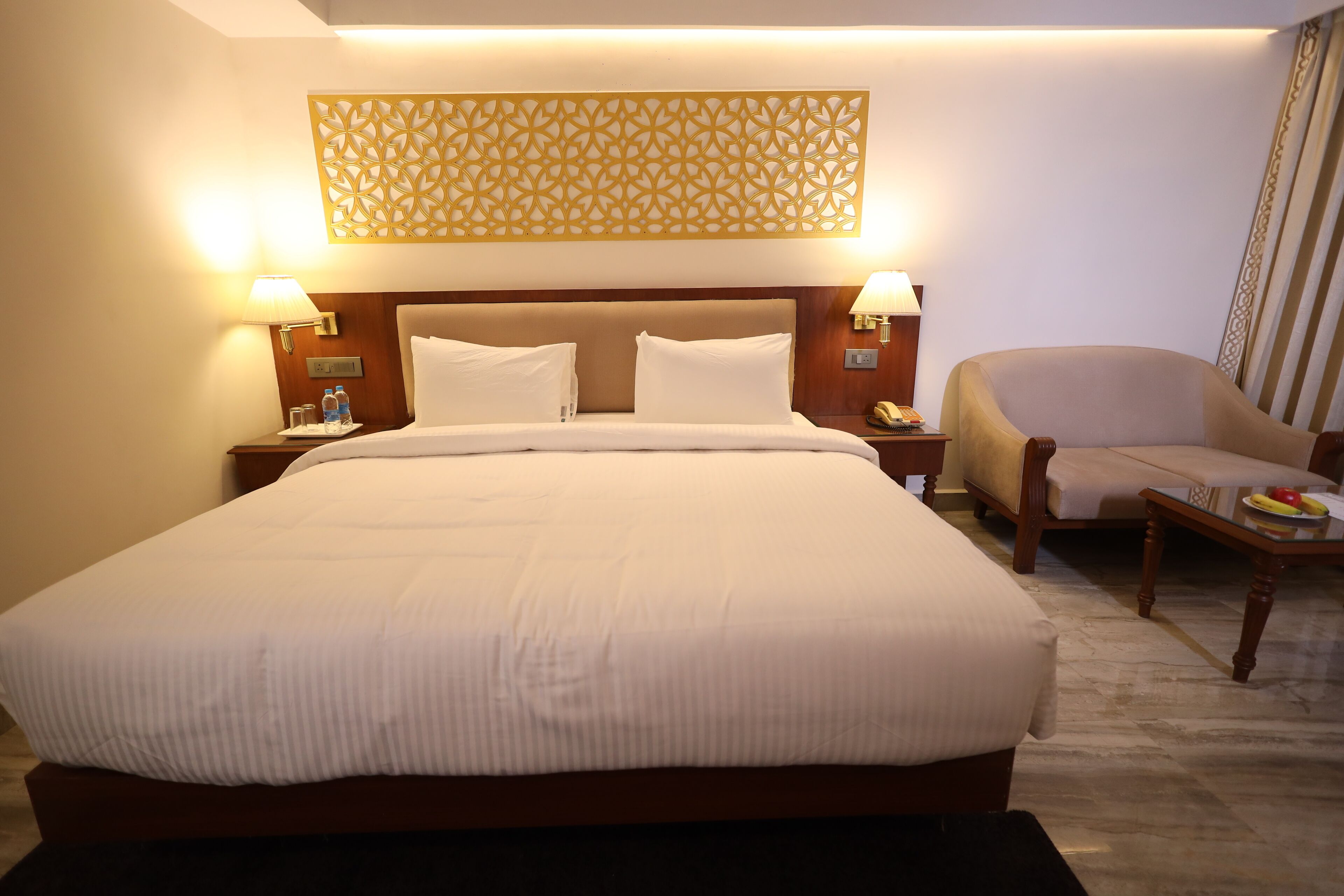 A hotel room with a large bed, two bedside tables with lamps, a chair, and a decorative wall piece.