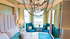 A hotel room with a large bed, two blue armchairs, a chandelier, and a view of the outdoors through the window. - Thornton Hall Hotel and Spa (Wirral)