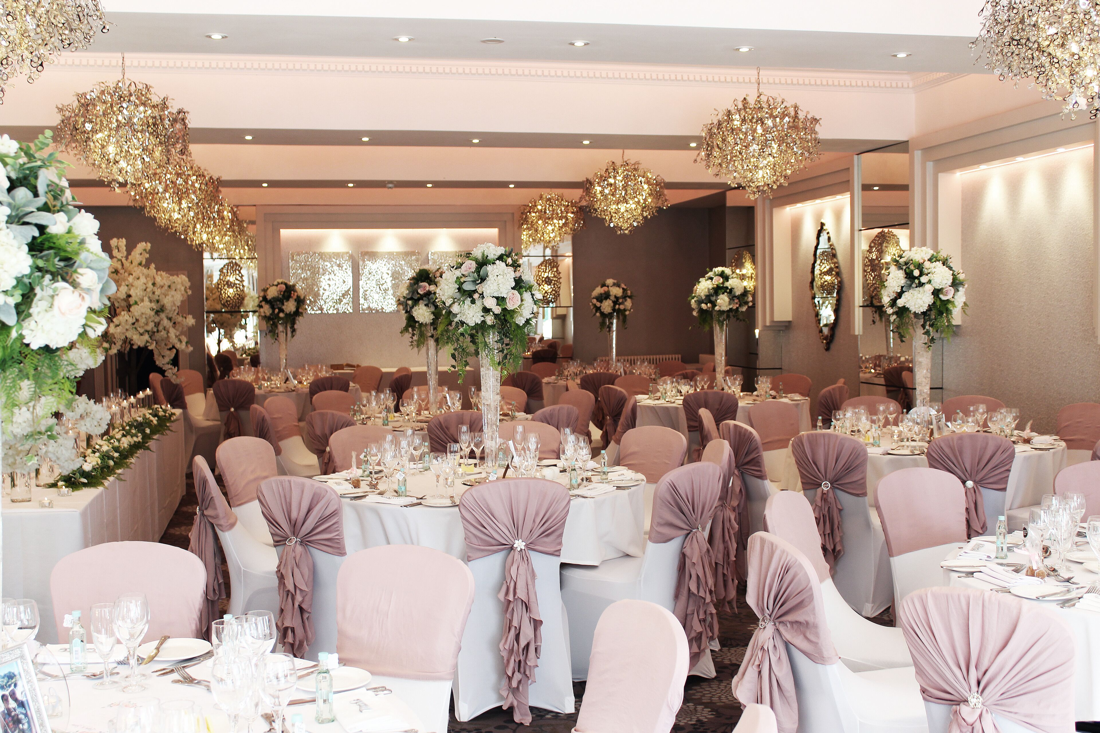 A banquet hall with round tables, chairs, and floral centerpieces.