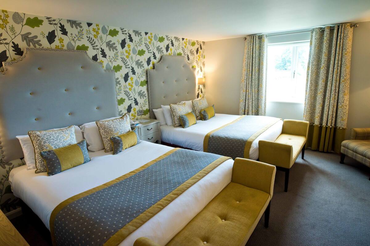 A hotel room with two beds, a sofa, and a window with curtains.