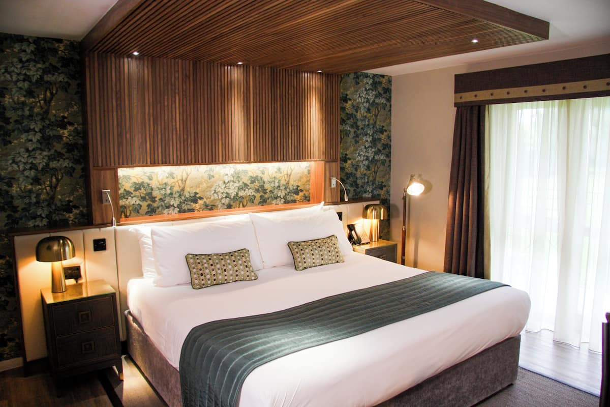 A large bed with a wooden headboard, two bedside tables with lamps, and a floral wallpaper design.