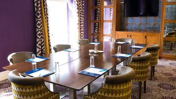 Un salón de conferencias con una mesa larga, sillas, un televisor y cortinas estampadas.