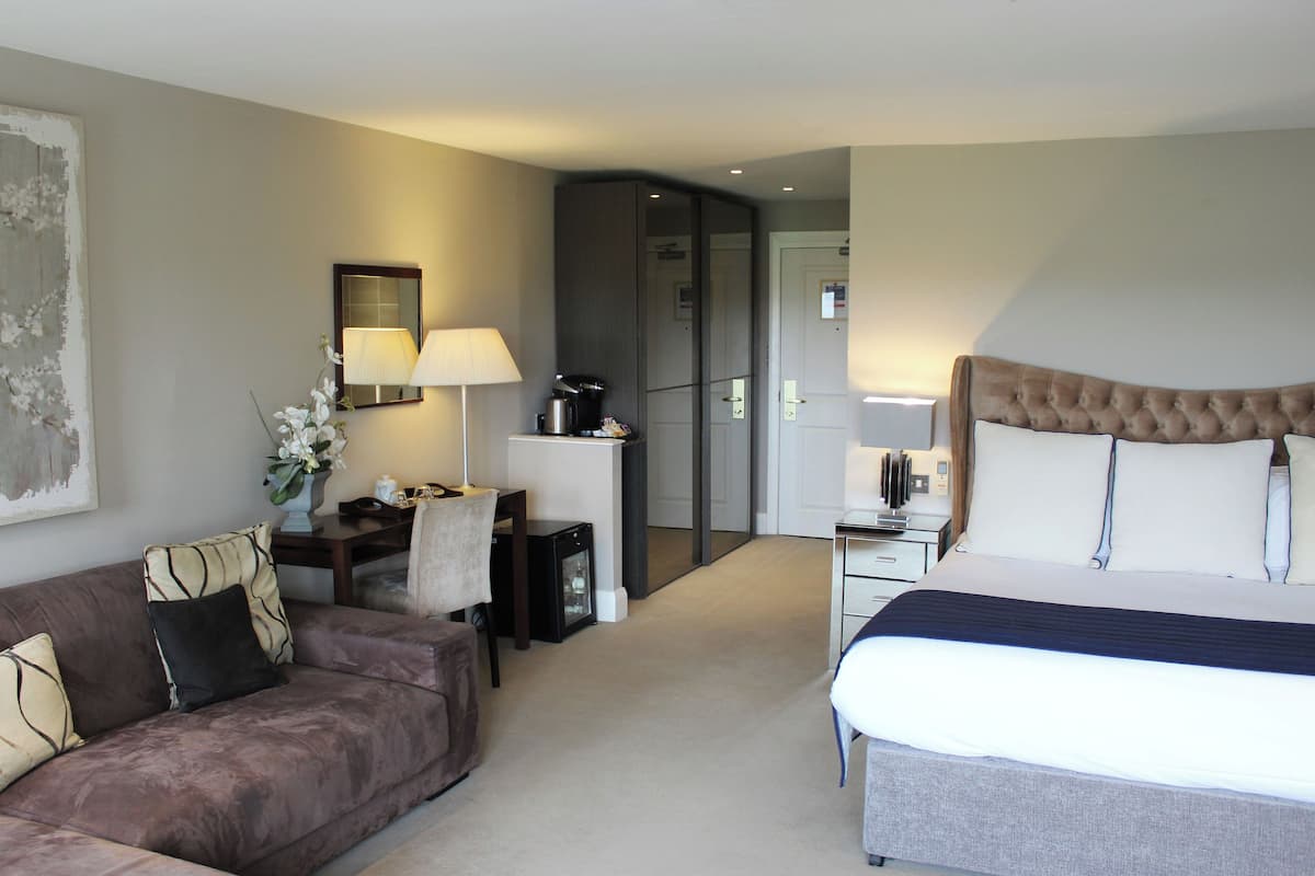 A hotel room with a bed, a sofa, a desk with a lamp, and a coffee maker.