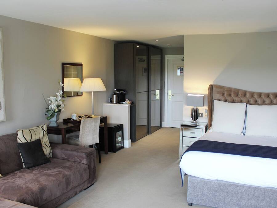 A hotel room with a bed, a sofa, a desk with a lamp, and a coffee maker.